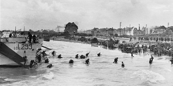 LCIL 299 has hit a mined beach obstacle and has grounded short.  (She was later floated off and sailed back to England.)  Bicycles being carried by disembarking troops are getting a good salt-water soaking.  The prominent house in centre (left end of the beach) was the first house in Bernières-sur-Mer to be liberated by Canadian soldiers in the opening minutes of the landing.  The family continues to maintain it as "Canada House" after the death of the owner.
Photo Credit: Imperial War Museum