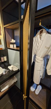 Two robes, slippers and a laundry bag in a cupboard that opens bed and bathroom sides