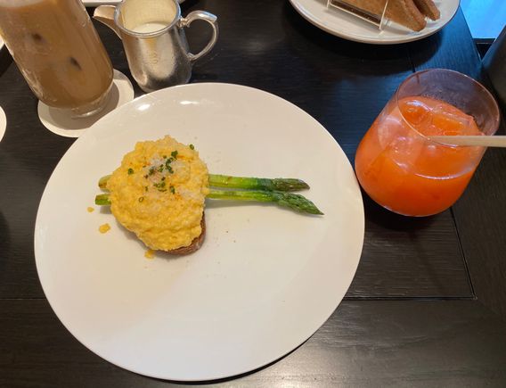 Scrambled eggs on country bread with asparagus , along with fresh carrot , orange and watermelon juice ; iced latte 