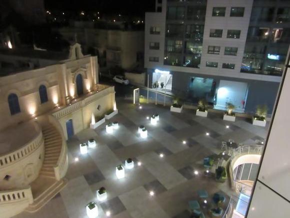 View from the balcony onto the main entrance "square" -- the grey building across the street is Bay Street complex, and if you took the lift to the 3rd floor and made a left U-turn, you would emerge from the white-lit entrance on the left. Seed restaurant outdoor seating visible on the right of this photo.