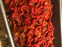 In the loaf pan with a jacket of tomatoes and  squiggles of tomato paste. 