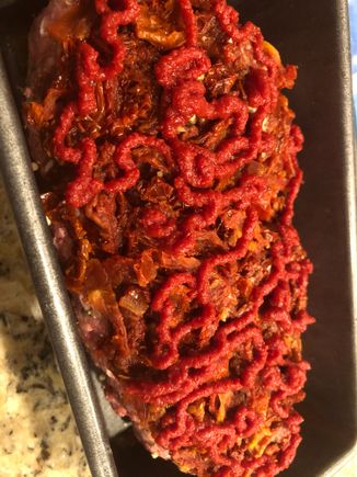In the loaf pan with a jacket of tomatoes and  squiggles of tomato paste. 