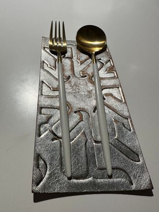 One of many place settings; sleek modern utensils sit atop embossed leather mats; this one was metallic silver; others were deep forest green and other colors..
