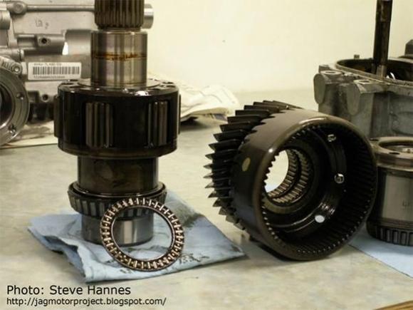 The assembly seen below the main drive gear on the mainshaft is the planetary gear set. This is the assembly that "splits" the incoming torque from the transmission into the 61%/39% ratio. Here is what the gearset looks like:  Look closely and you can see the planetary gears in a carrier on the mainshaft. Next to it on the right is the mating gear housing. Essentially the way this works is: The mainshaft on the left is actually two shafts, one inside another. The outside shaft receives all of the torque from the transmission output.